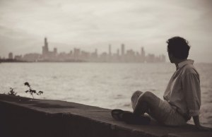 man sitting on ledge by water and a city.