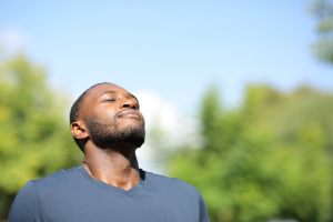 Man outside with his eyes closed facing the sky.