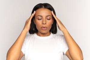 Woman in a white t-shirt rubbing her temples to relieve stress in front of white background.