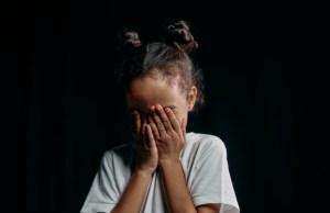 Little girl with face in Little girl holding her hands on her face in front of a black background.