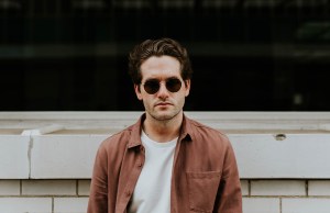 Man with sun glasses on staring forward with a neutral face.