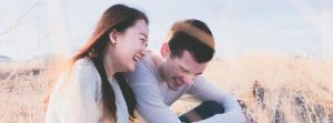 Man & woman sitting and laughing outside with tall grass.
