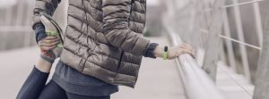 Woman stretching & leaning on a railing outside wearing a jacket.