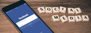 Phone with Facebook log in showing next to scrabble tiles that spell out social media.