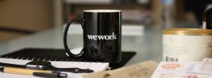 "Wework" mug on surface of desk in focus.
