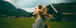 Side profile of woman smiling with her hair blowing standing in front of a scenic background.