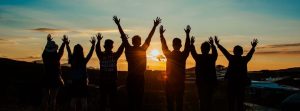 Group of people with there arms up looking at the sunset.