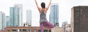 Woman stretching & posing with her arms up looking out at the city line.