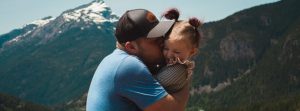 Man holding and kissing his daughter in front of scenic mountains.