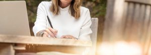 Woman writing with a pen sitting outside.