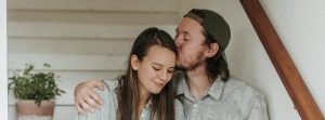 Man kisses woman's head while sitting on the stairs.