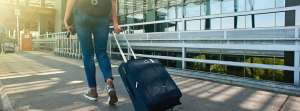 Woman walking on the sidewalk rolling a suitcase behind her.