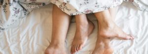 Close up of couples feet in bed together under the covers.