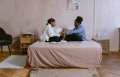 Two women sitting cross legged on bed holding hands.