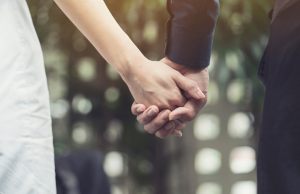 Close up of bride and groom holding hands.