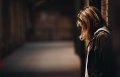 Woman leaning against wall looking down.