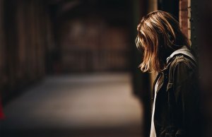 Woman leaning against wall looking down.