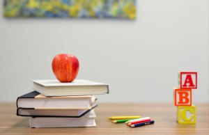 Stacked books with red apple and abc blocks on desk.