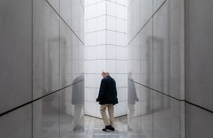 Older man walking between white walls.