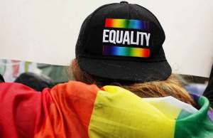 Person wearing a lgbtq flag & a backwards hat that says equality.