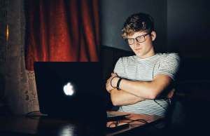 Man in striped shirt looking at apple laptop.
