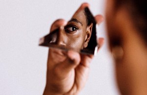 Person holding broken mirror looking at themselves in the reflection.