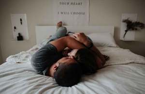 Man and woman hugging and laying down on white bed.