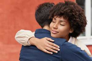 Two people hugging in front of a red building