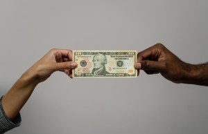 Black hand and white hand exchange 10 dollar bill.
