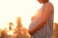 A pregnant woman holding her belly at sunset.
