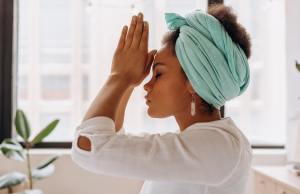 Woman meditates with eyes closed and praying hands in green turban.