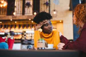 Woman in a yellow sweater sitting in a restaurant being comforted by a friend