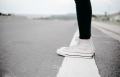 Someone stands on a white road line in white converse high tops.