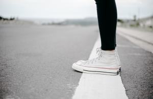 Someone stands on a white road line in white converse high tops.