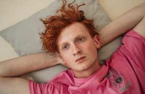 Young man deep in thought laying on a pillow in a pink tee shirt.