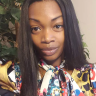 Khadija Tuitt Woman smiling indoors, wearing a colorful scarf, standing near green plants