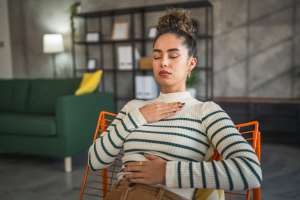 Woman in a striped sweater sitting in an orange chair doing breathing exercises