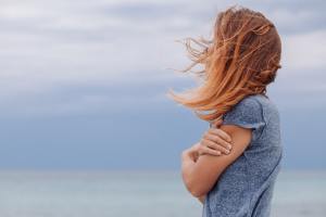 Side profile of woman holding her arm with her hair blowing over her face.