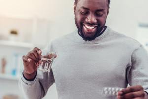 Man smiling holding a glass of water & pills.