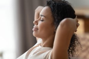 Relaxed woman leaned back with hands behind her head & eyes closed.