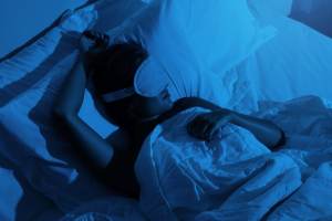 Woman sleeping with a blindfold on in a dark room.