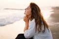 Woman sitting and thinking on the beach with her eyes closed.