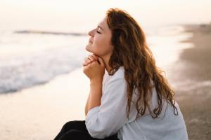 Woman sitting and thinking on the beach with her eyes closed.