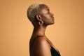 Woman's side profile standing against a orange/yellow background.