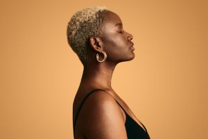 Woman's side profile standing against a orange/yellow background.