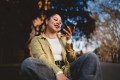 Woman sitting outdoors looking at phone with confident smile, representing setting healthy boundaries during the holidays