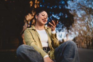 Woman sitting outdoors looking at phone with confident smile, representing setting healthy boundaries during the holidays