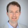 Alex Evans, pharmacist and medical writer, looking at the camera on a light gray background