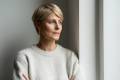 Blonde middle-aged woman in a gray sweater looking out a window