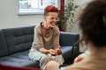 Person with red hair sitting on a gray couch talking to a therapist